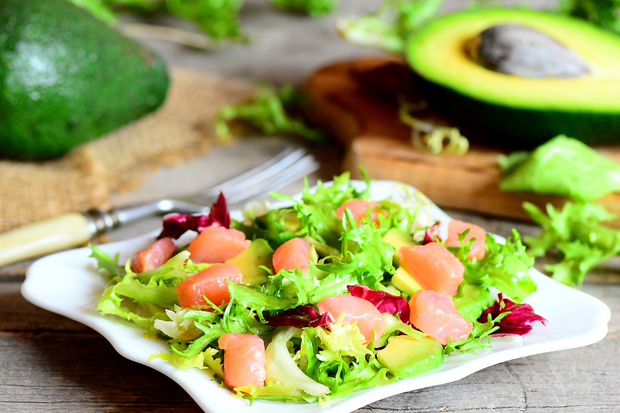Salmon, avocado and mixed lettuce salad recipe. Easy salad with salmon slices, fresh avocado and lettuce leaves mix on a plate. Avocado, fork on a vintage wooden table. Closeup