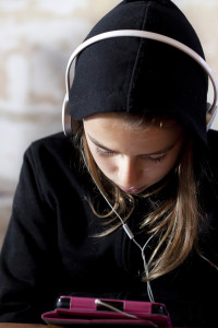 A teenager looking down on a tablet listening to music.
